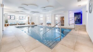 A modern indoor swimming pool with a clear view of the pool area, a staircase leading to a higher level, and a large wall clock. - Ruhpoldinger Hof (Ruhpolding)