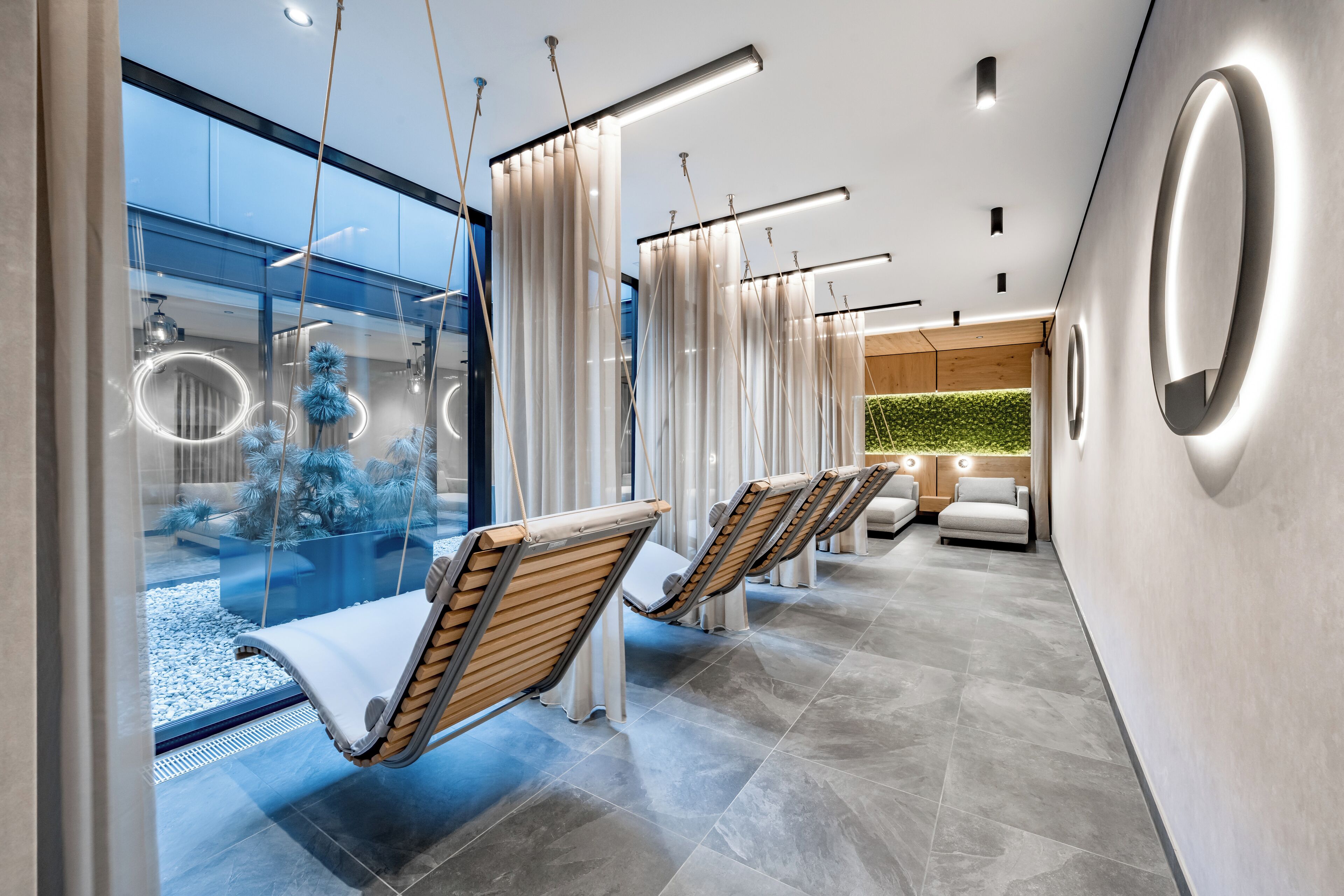 Ein moderner Spa-Bereich mit Hängestühlen, einer Glaswand mit Aussicht und einer begrünten Wand.