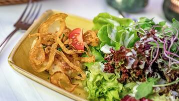 Un plato rectangular con una ensalada de lechuga, tomate y posiblemente algunos brotes, acompañado de aros de cebolla fritos.
