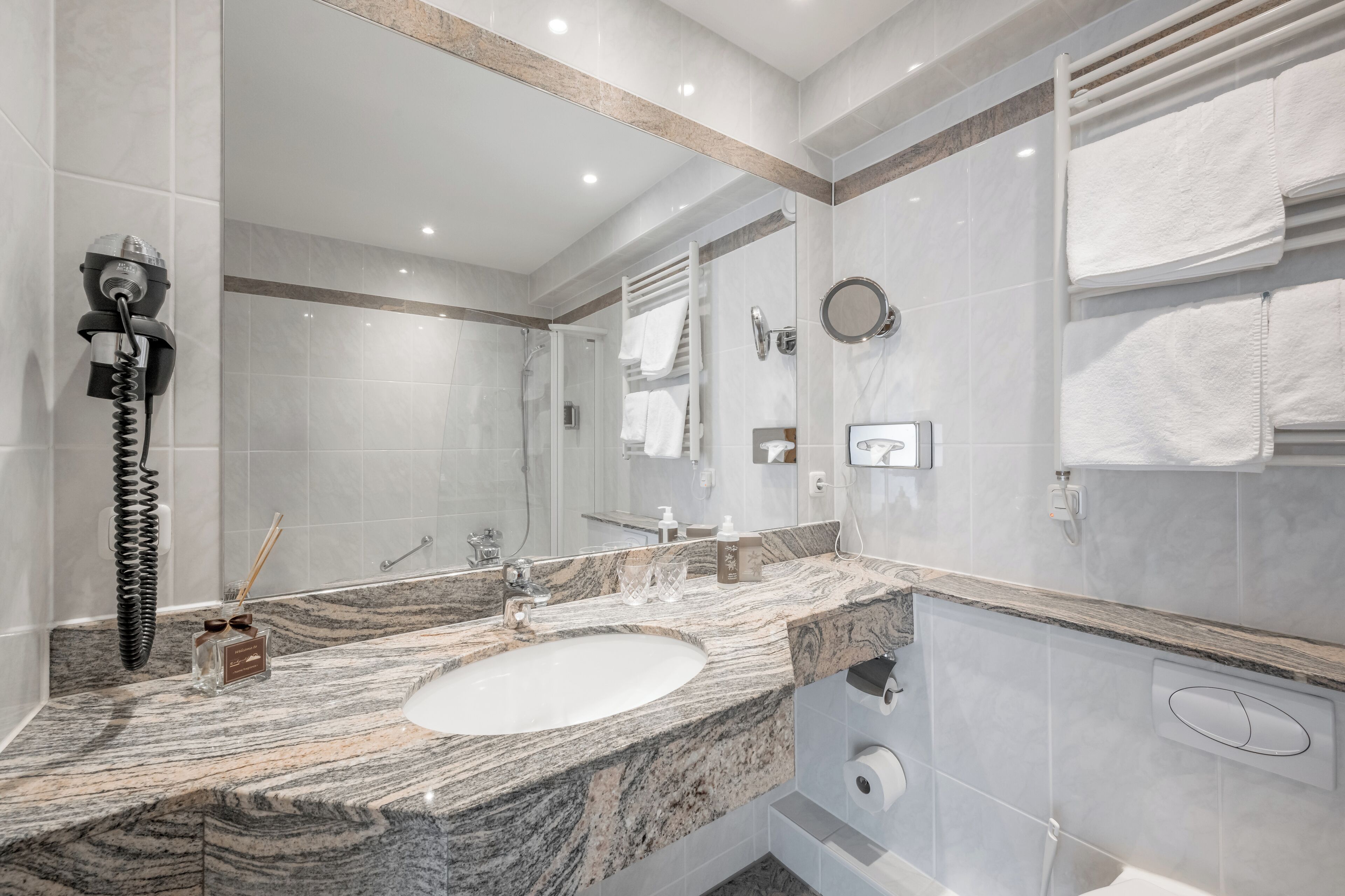 Un baño moderno con un lavabo de mármol, un espejo grande y un perchero para toallas.