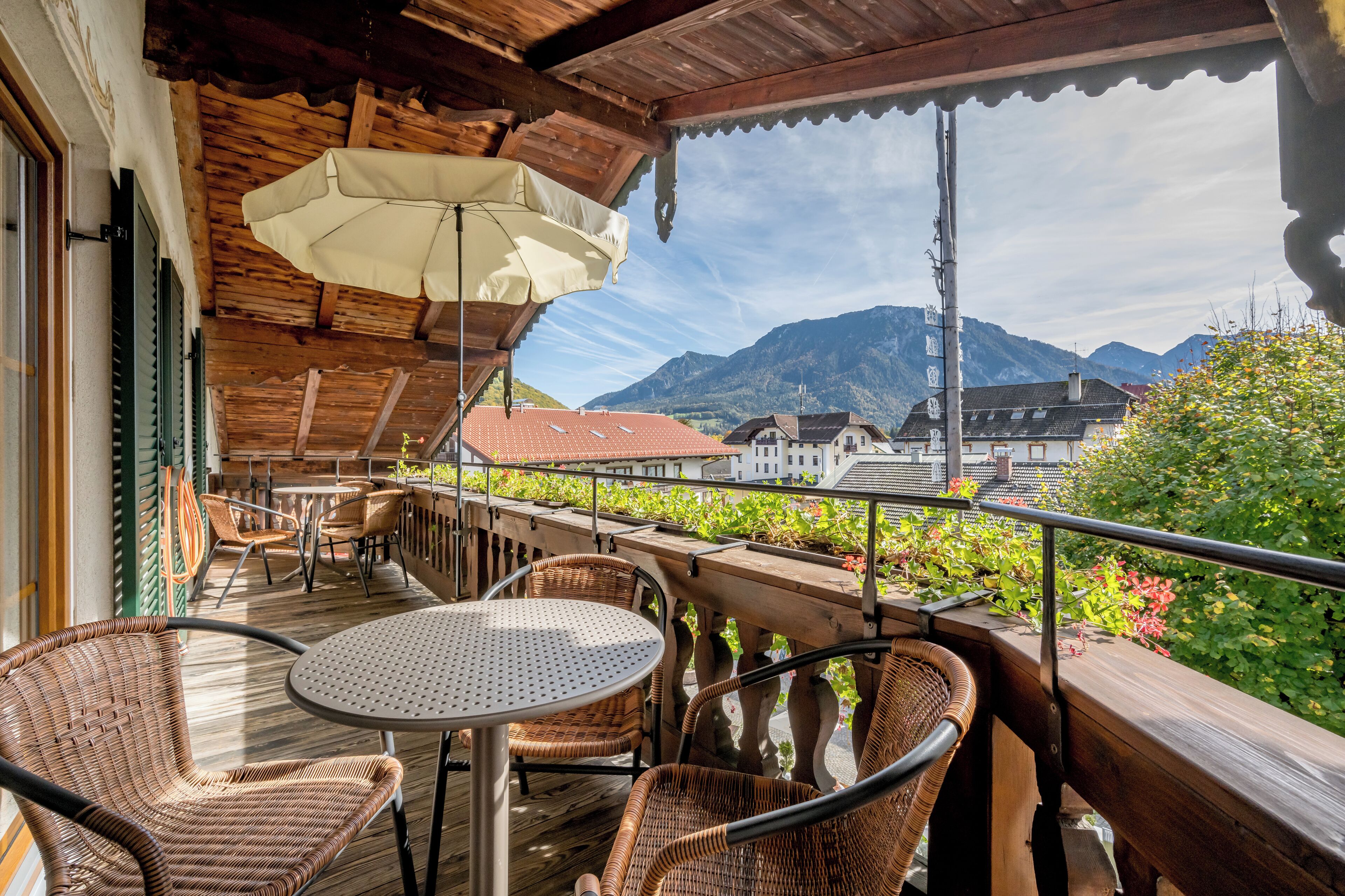 A wooden deck with wicker chairs and a round table, overlooking a mountain landscape.