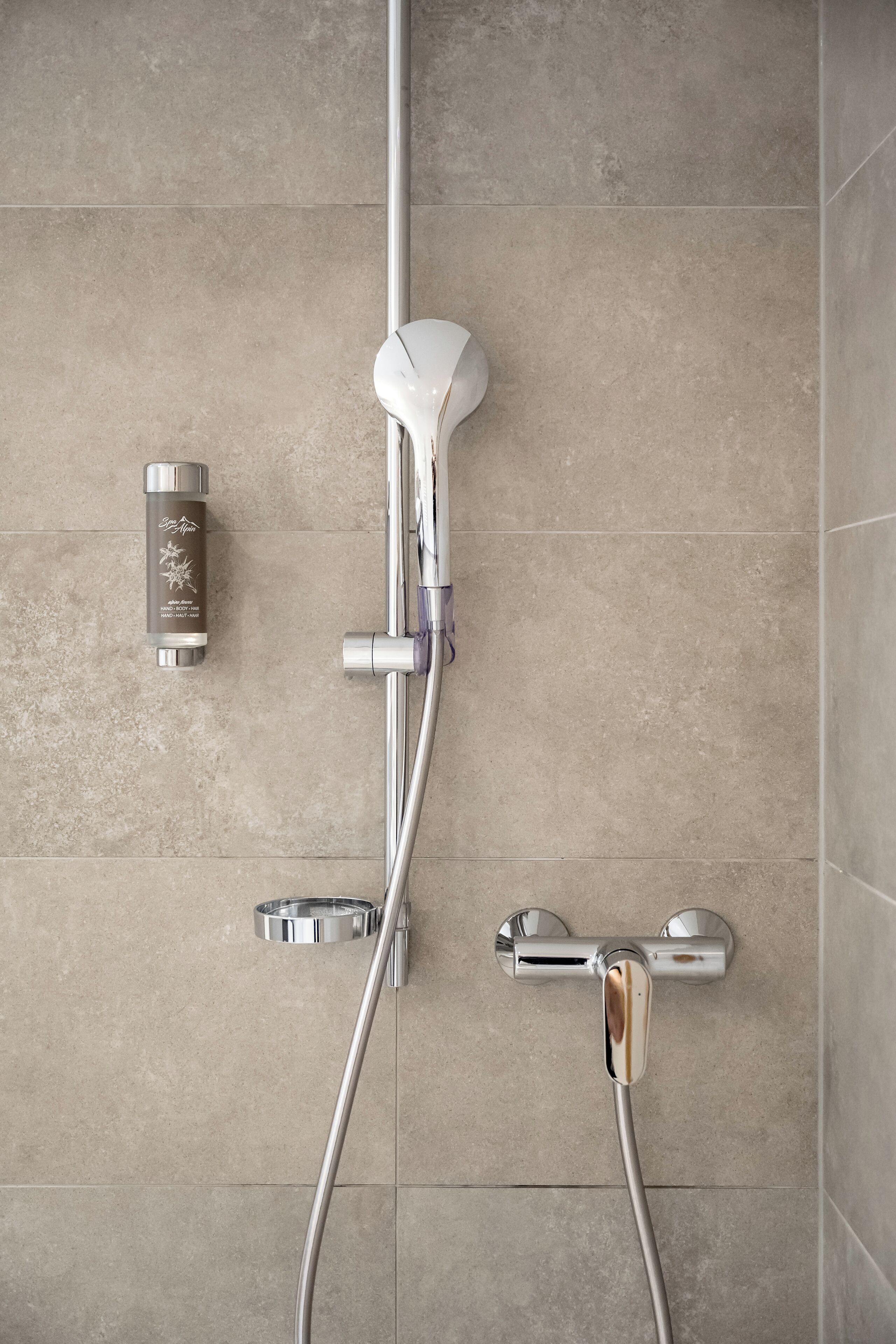 Een moderne badkamer met een douche, een handdouche en een wandmengkraan.