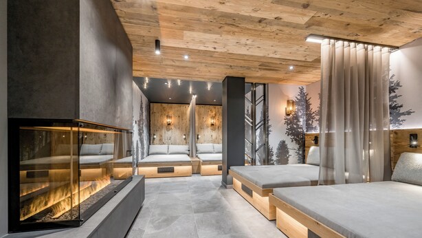 A modern interior with a fireplace, built-in seating, and a large window with a forest mural. - Ruhpoldinger Hof (Ruhpolding)