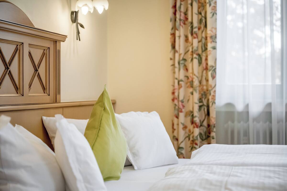 A neatly made bed with white and green pillows, a wooden headboard, and a floral curtain.