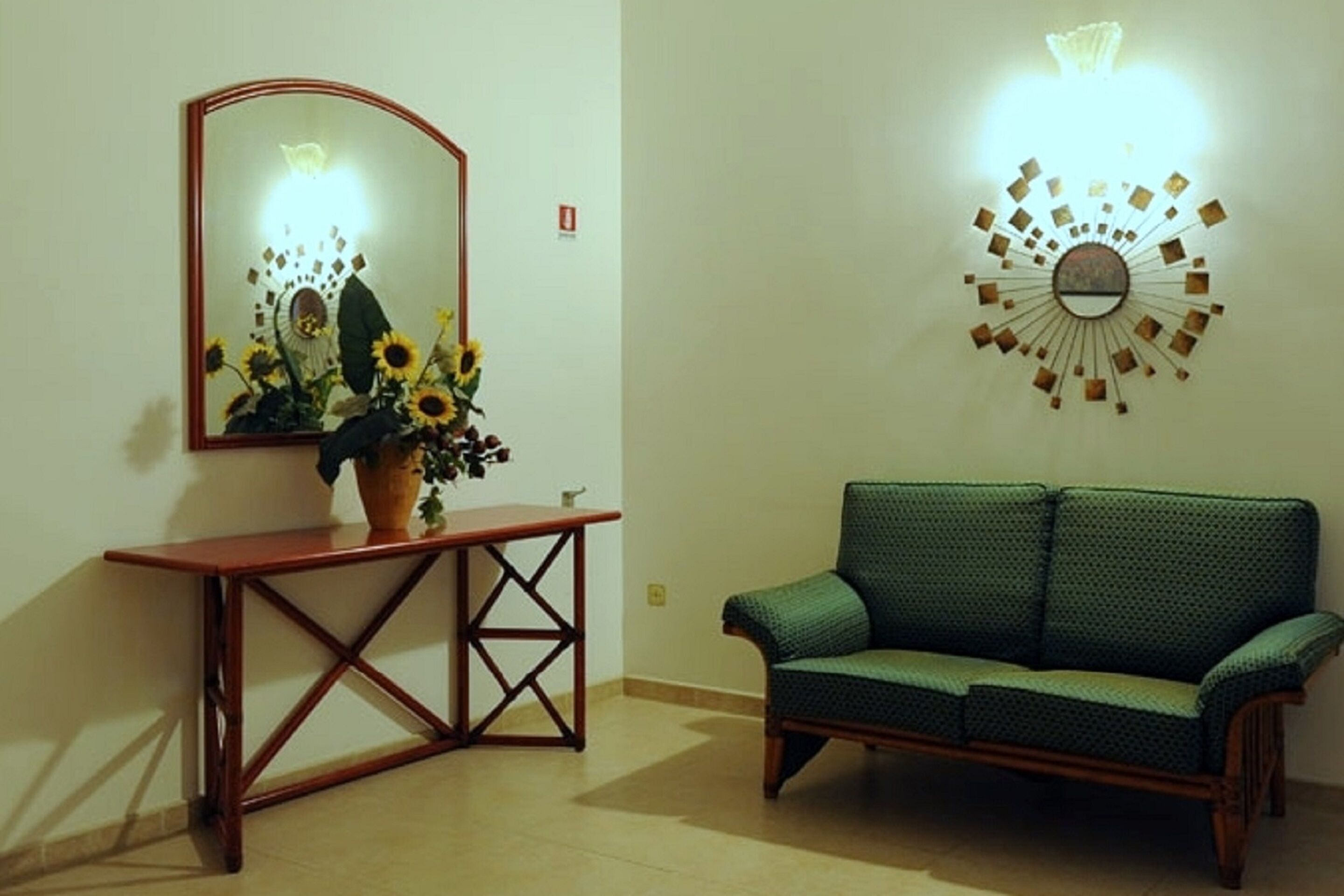 A room with a wooden console table, a green sofa, a wall-mounted mirror, and a decorative wall light.