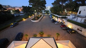 A parking area with cars, a landscaped garden, and buildings in the background. - Hotel Villa Rosa (Martina Franca)