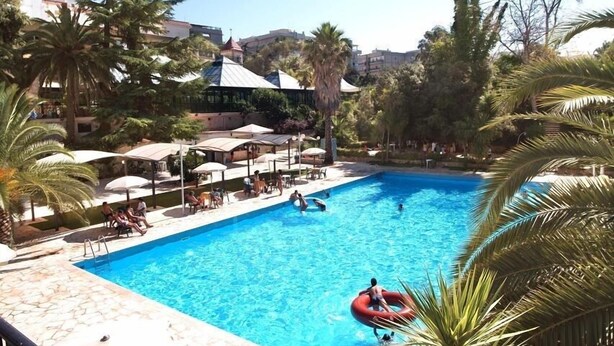A swimming pool with lounge chairs and umbrellas, surrounded by palm trees and buildings. - Hotel Villa Rosa (Martina Franca)
