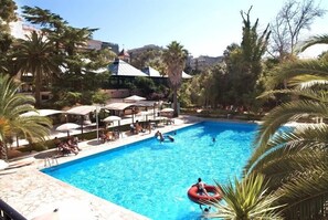 A swimming pool with lounge chairs and umbrellas, surrounded by palm trees and buildings. - Hotel Villa Rosa (Martina Franca)