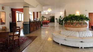A spacious lobby with a round white sofa, a reception desk, and a large decorative planter. - Hotel Villa Rosa (Martina Franca)