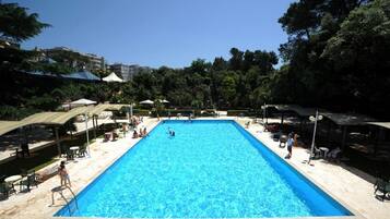 Ein rechteckiger Swimmingpool mit klarem, blauen Wasser, umrahmt von Steinplatten und beschattet durch Sonnenschirme.