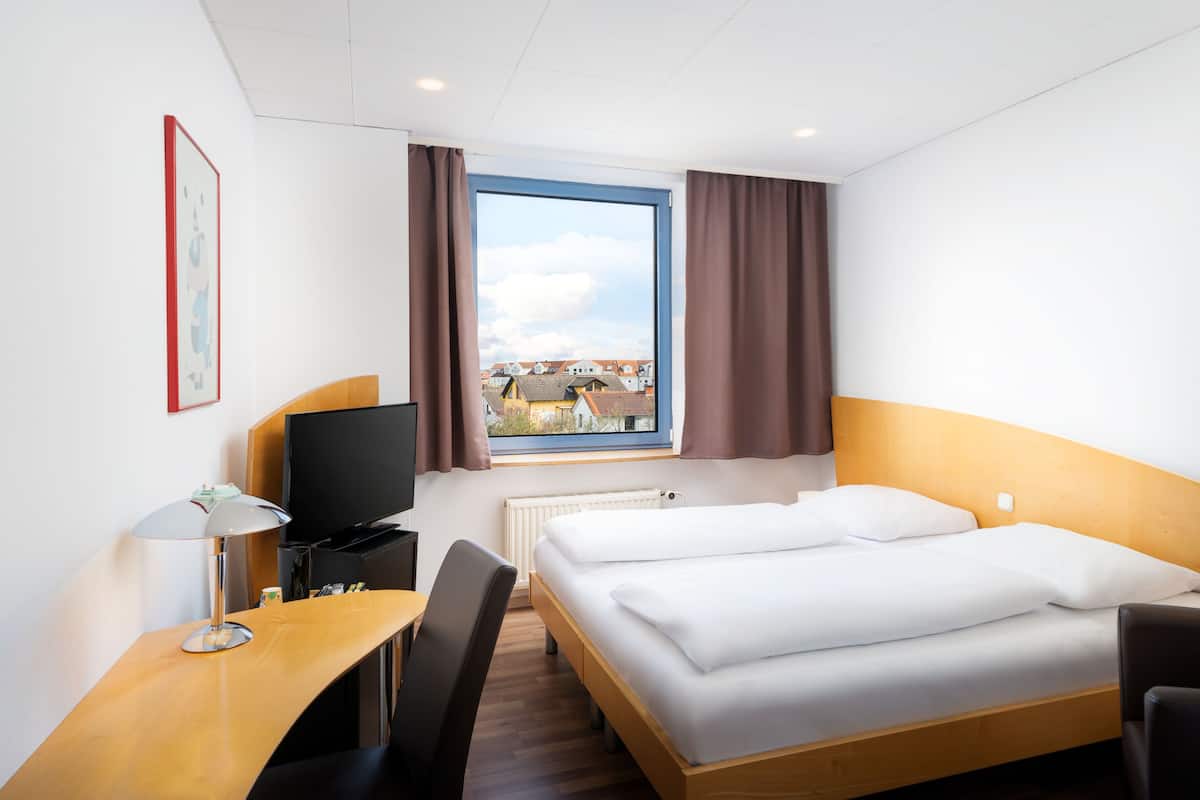 A hotel room with a bed, desk, chair, TV, and a window with curtains.