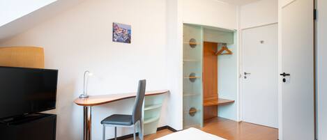 A modern hotel room with a bed, a desk with a chair, a TV, and a walk-in closet.