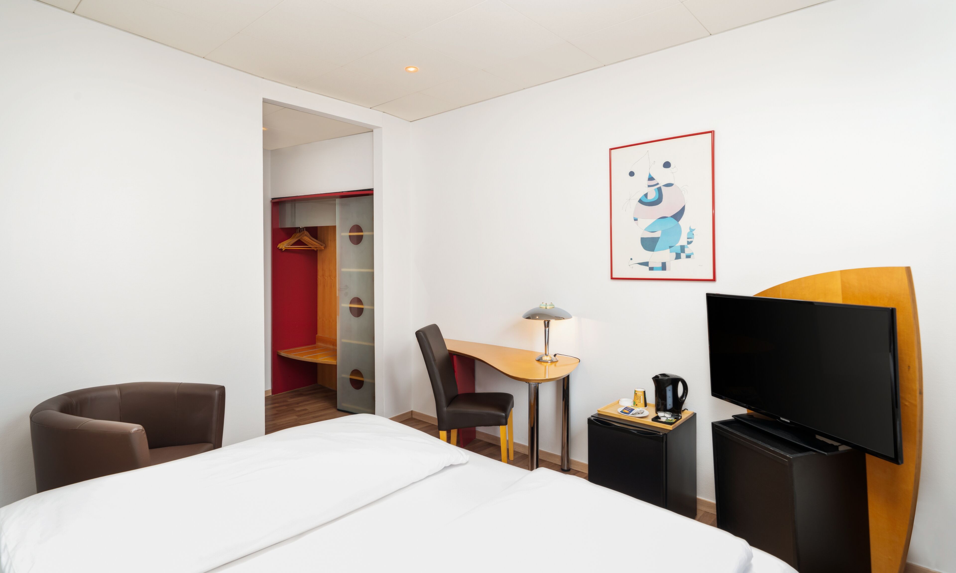 A hotel room with a bed, a desk, a chair, a TV, and a wardrobe.