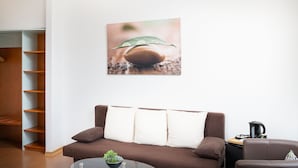 A modern living room with a brown sofa, a glass coffee table with a plant, and a wall-mounted picture of a snail on a leaf. - Hotel Mainstreet (Dietzenbach)