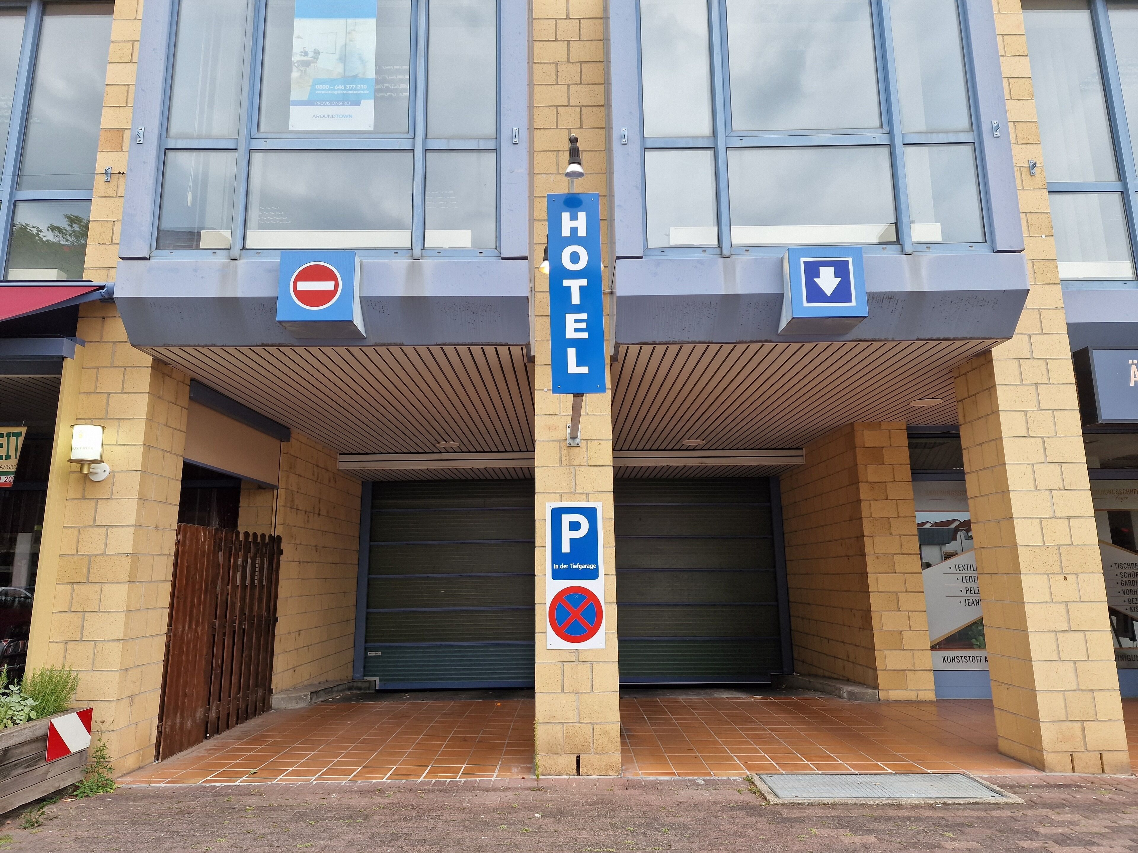 A hotel entrance with a closed garage door, a no parking sign, and a directional sign for the hotel.