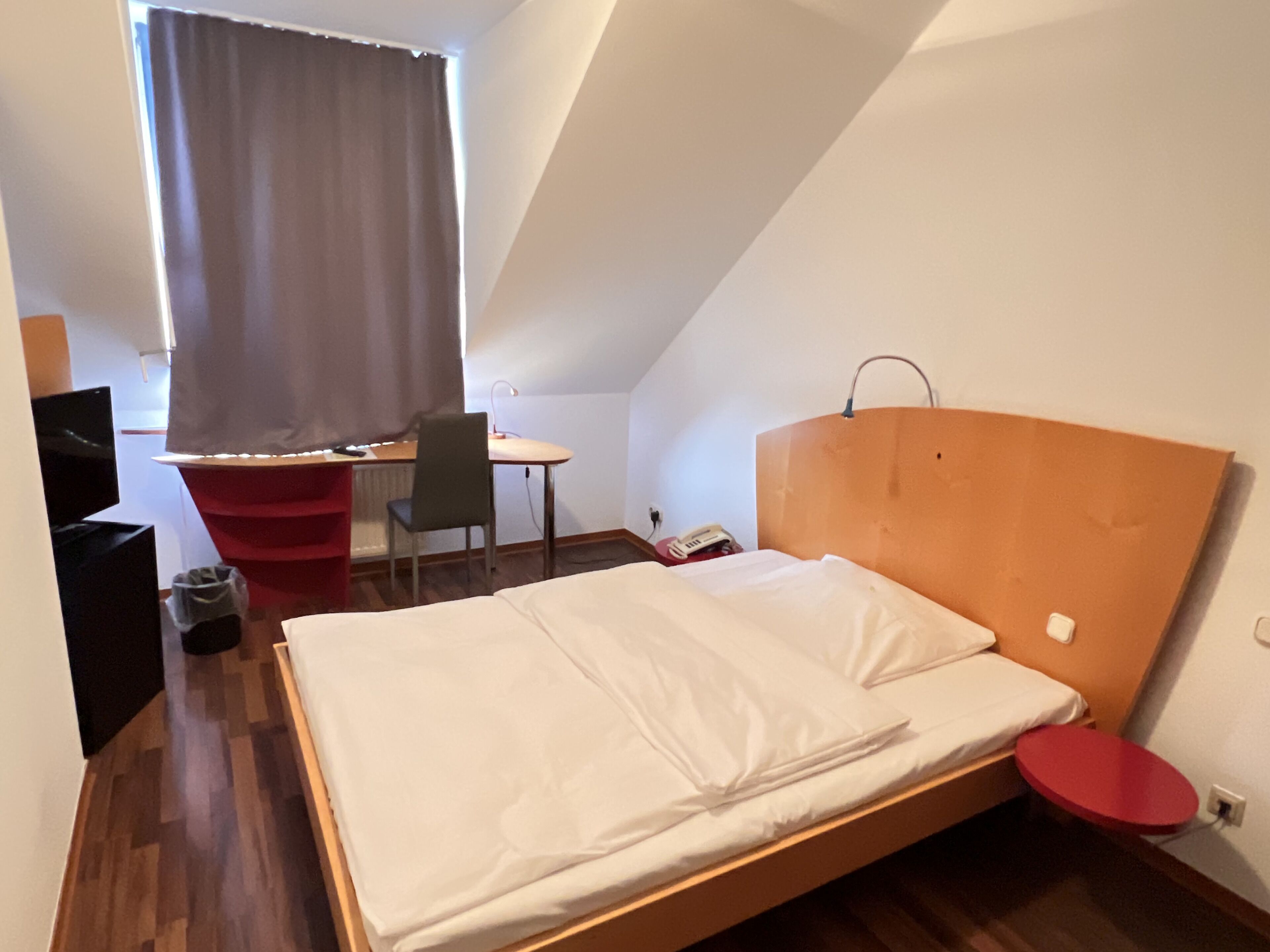 Quarto pequeno e moderno com uma cama, uma escrivaninha e uma cadeira.