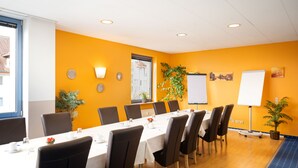 A conference room with a long table, chairs, a whiteboard, and potted plants. - Hotel Mainstreet (Dietzenbach)