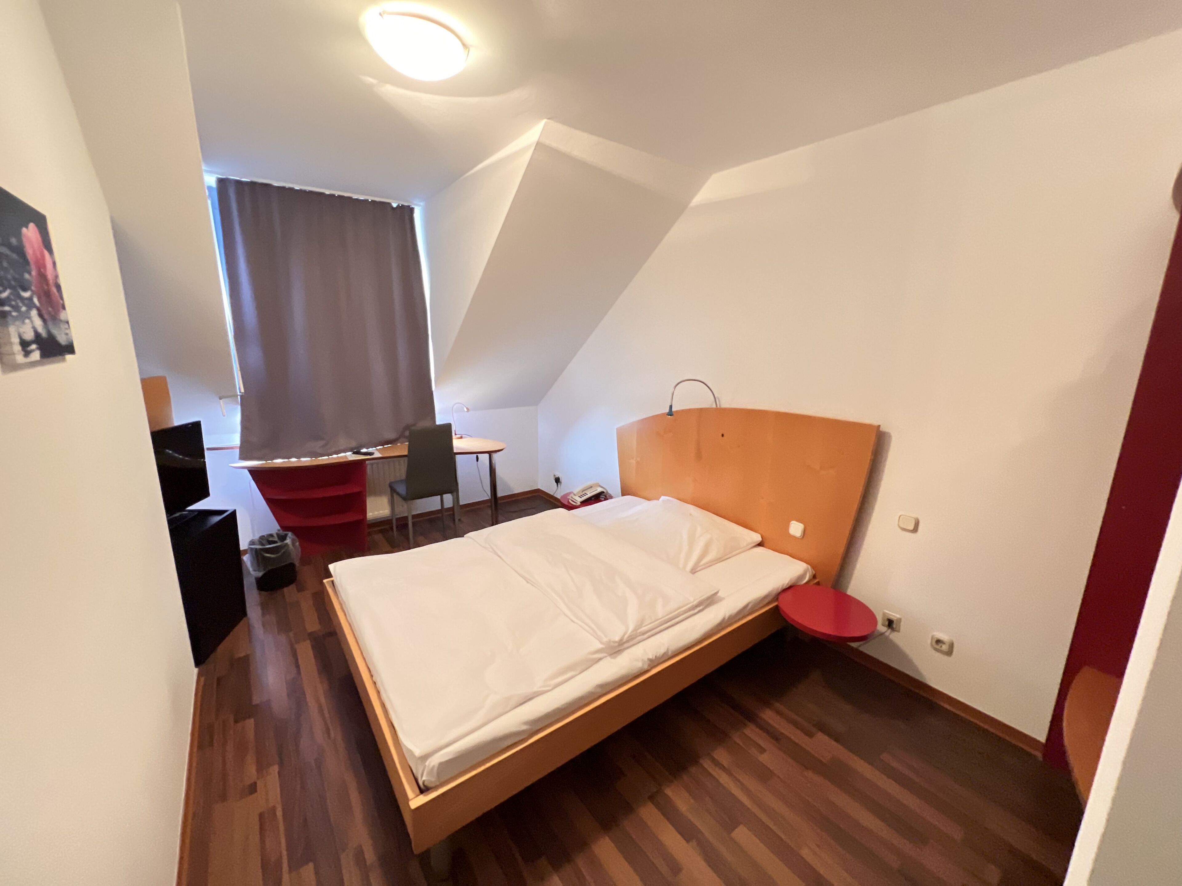 A small, modern room with a wooden bed, a desk, and a chair.