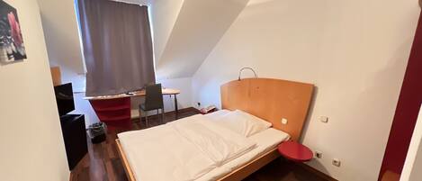 A small, modern room with a wooden bed, a desk, and a chair.