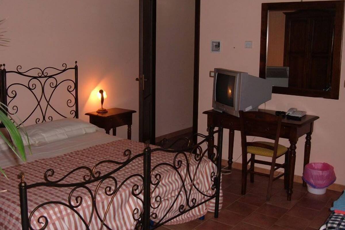 Ein Schlafzimmer mit einem Bett, einem Schreibtisch mit Fernseher, einem Sessel und einem Spiegel an der Wand.