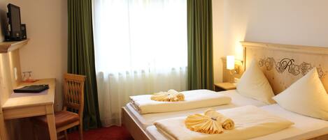 A hotel room with two beds, a desk, a chair, a TV, and a window with curtains.