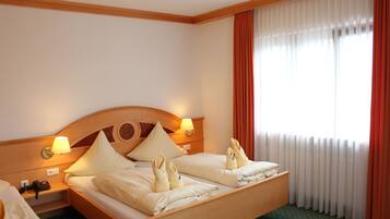 A hotel room with a wooden headboard, two bedside lamps, a bed with towels, a telephone, and a window with curtains.