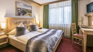 Ein Hotelzimmer mit einem hölzernen Bett, einem Schreibtisch, einem Sessel, einem Fernseher und einem Gemälde an der Wand.