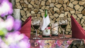 Ein Tisch mit zwei Weingläsern, einer Flasche und einer Kerze, vor einer Kulisse aus gestapeltem Holz und einem herzförmigen Spiegel.