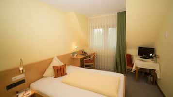 Una habitación de hotel con cama, escritorio, silla, televisor y ventana con cortinas.