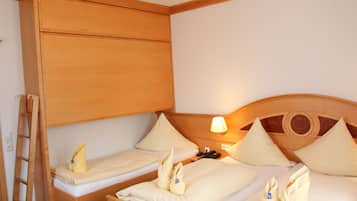 Une chambre d’hôtel avec deux lits simples, des têtes de lit en bois, une armoire en bois, une table de chevet avec une lampe et une échelle appuyée contre le mur.