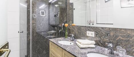 A modern bathroom with two sinks, marble countertops, wooden cabinets, and a large mirror.