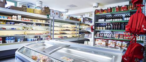 Un supermercado con secciones refrigeradas, estantes llenos de diversos productos, y una mochila roja colgada en la pared.