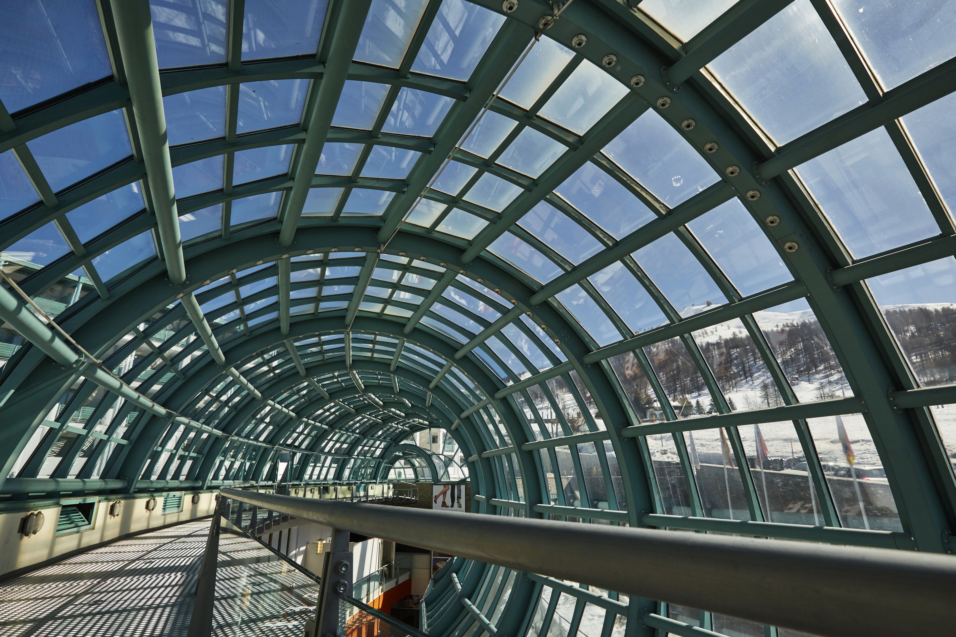 A glass-roofed corridor with metal railings and a view of a snowy landscape.