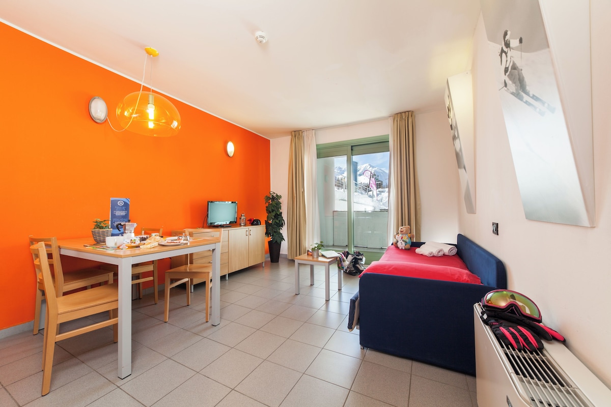 A hotel room with a dining area, a bed, and a view of the mountains.