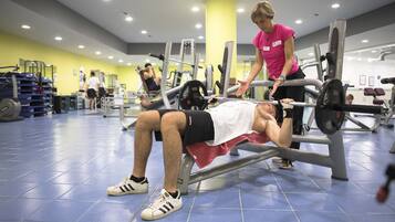 Una palestra con attrezzature per esercizi, una persona sdraiata su una panca e un'altra che sta aiutando.