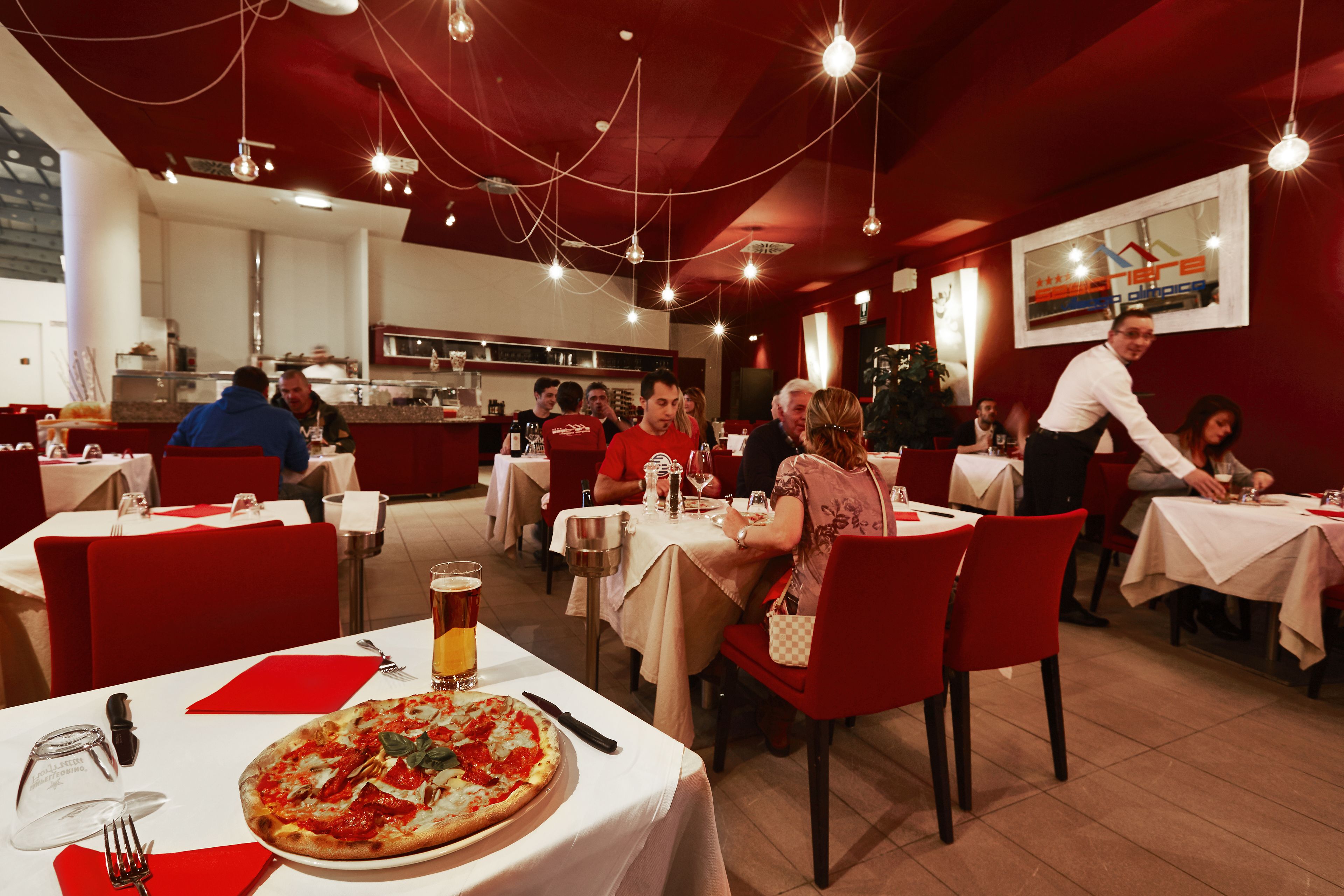 Un restaurant avec des tables dressées pour le service, une pizza sur l’une des tables et un bar en arrière-plan.
