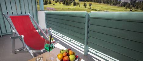 Un balcón con una silla roja, una mesa con una bandeja de frutas, un vaso de agua y una bebida.
