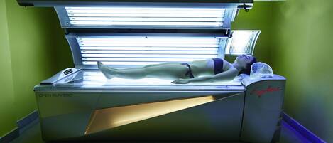 Uma cama de bronzeamento com uma pessoa deitada, um painel de controle e uma parede verde.