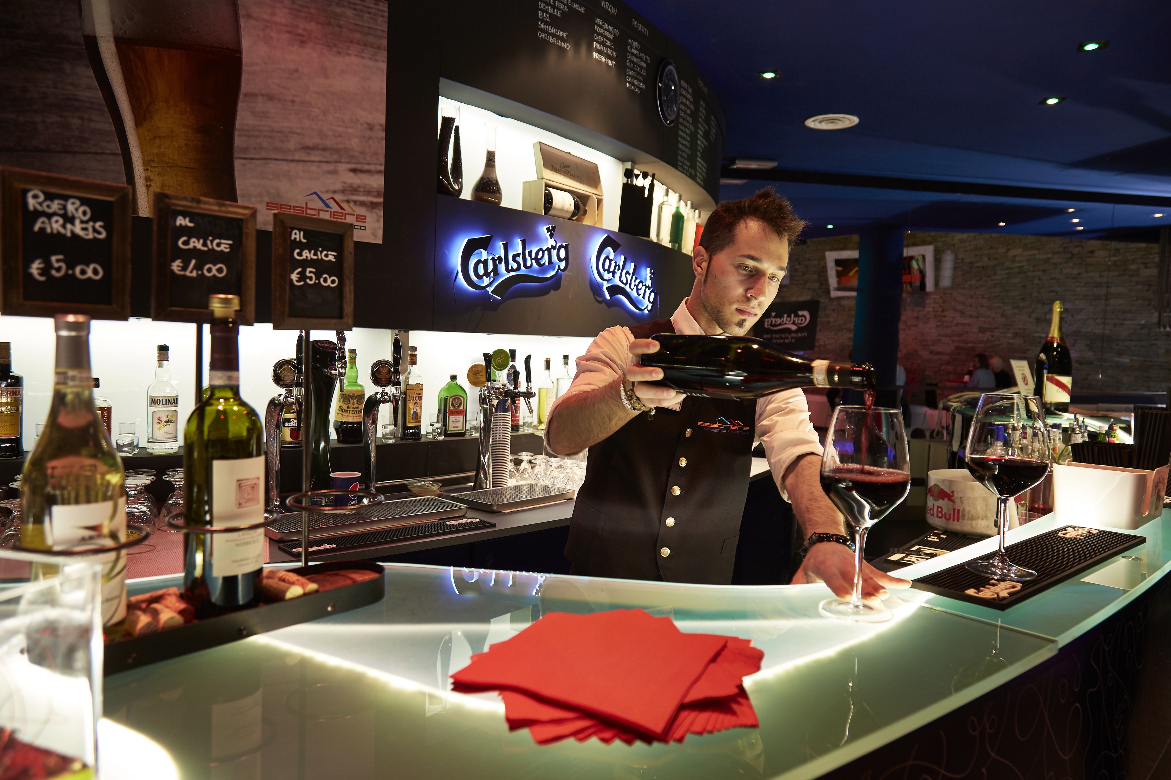 A bar area with a bartender preparing drinks, a menu board, and various bottles of alcohol.