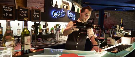 A bar area with a bartender preparing drinks, a menu board, and various bottles of alcohol.