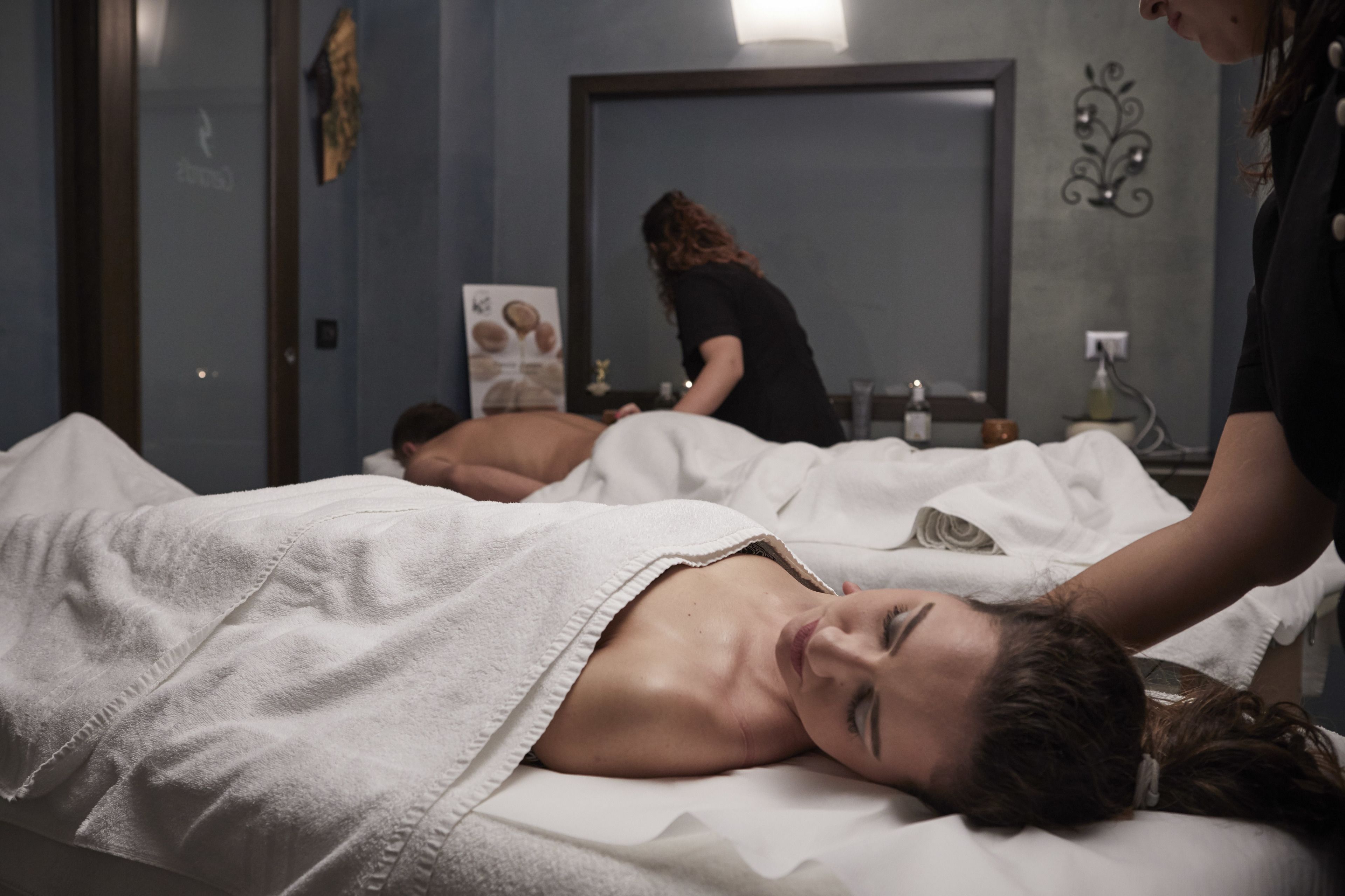 A spa room with a massage table, a massage therapist, and a client receiving a back massage.
