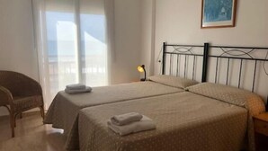 Une chambre d’hôtel avec deux lits, une chaise, une table de chevet avec une lampe et un tableau encadré au mur.