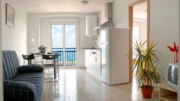 Un salon moderne comprenant un canapé, une table à manger avec des chaises, un coin cuisine avec un réfrigérateur et un balcon offrant une vue sur la mer.
