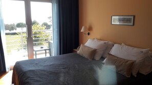 A hotel room with a bed, a nightstand, a lamp, and a view of a balcony with greenery. - Villa Rosetta (Umag)