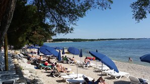 A beach with sun loungers and umbrellas, a rocky shoreline, and a calm sea. - Villa Rosetta (Umag)