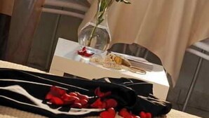 A table with a vase of a single rose, scattered rose petals, and a box of chocolates. - Villa Rosetta (Umag)