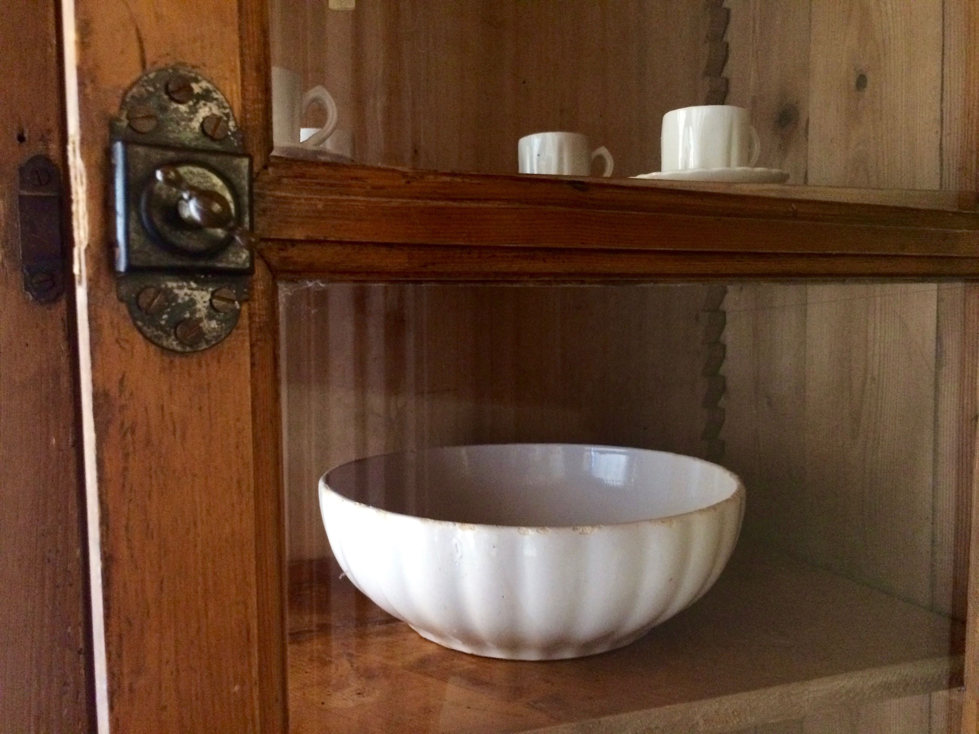 A wooden door with a glass panel, a white ceramic bowl, and two white cups on a shelf.