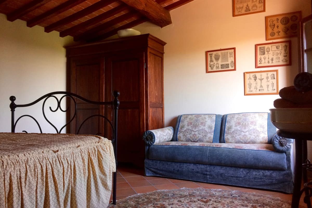 A bedroom with a bed, a wooden wardrobe, a sofa, and a patterned rug.