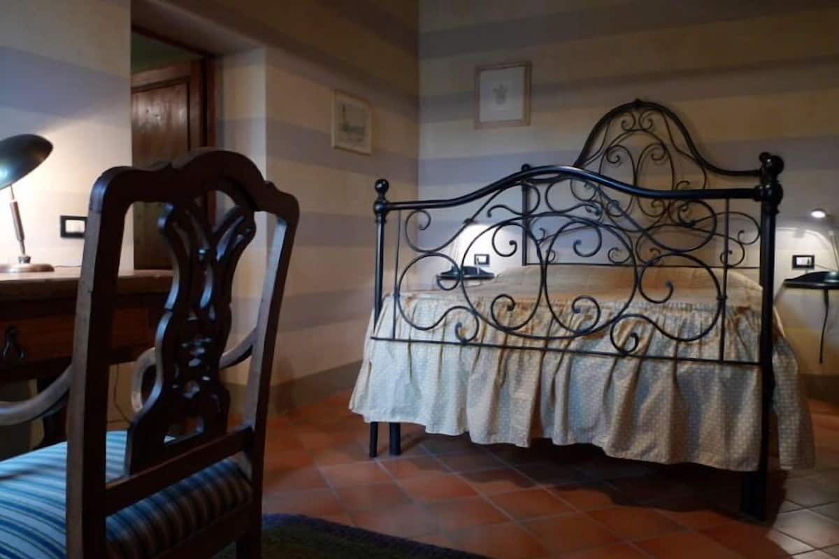 A bedroom with a metal bed frame, a wooden chair, a desk, and a tiled floor.