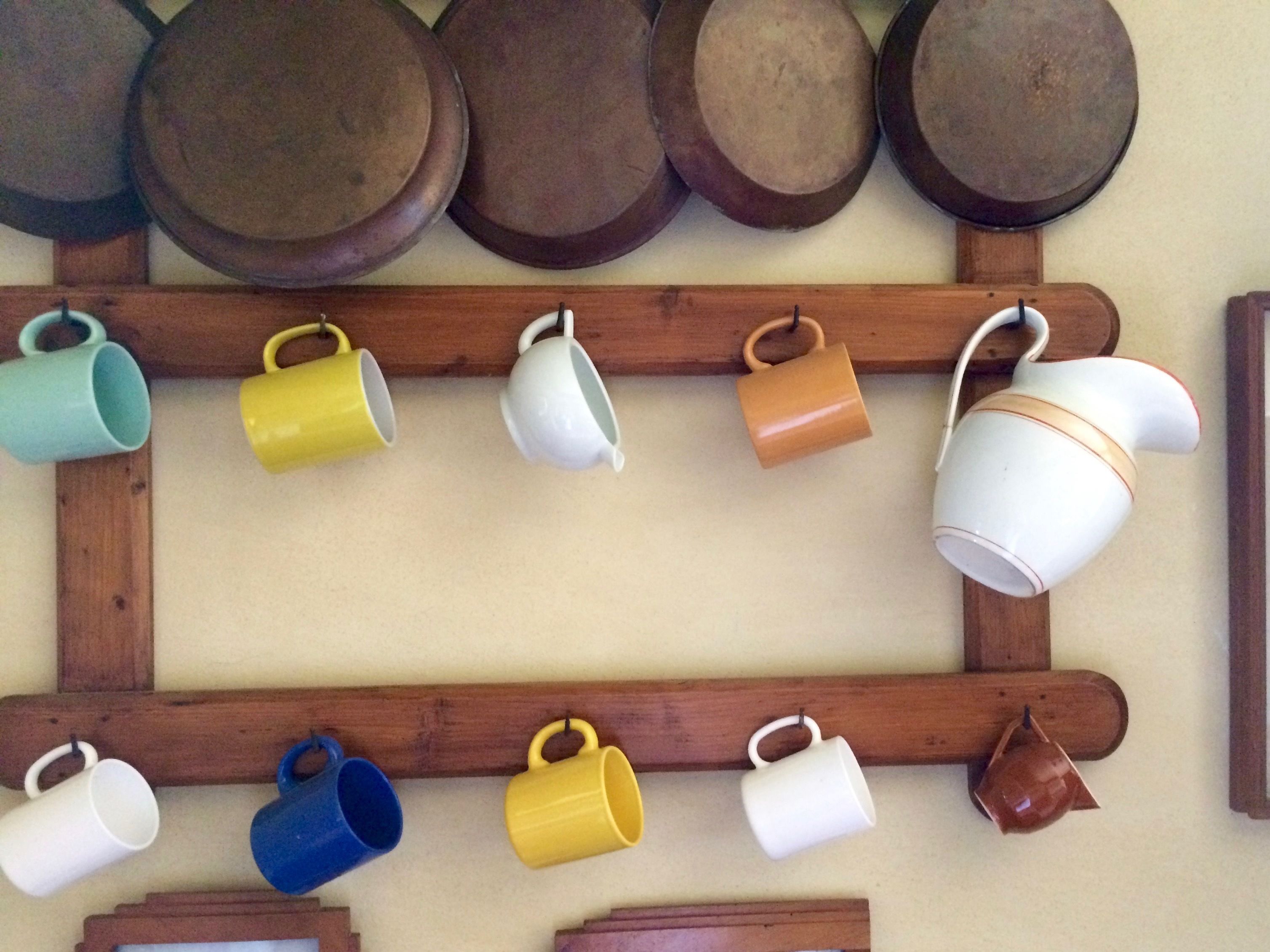 A wall with various kitchen utensils and cookware, including pots, pans, and mugs, arranged on wooden racks.